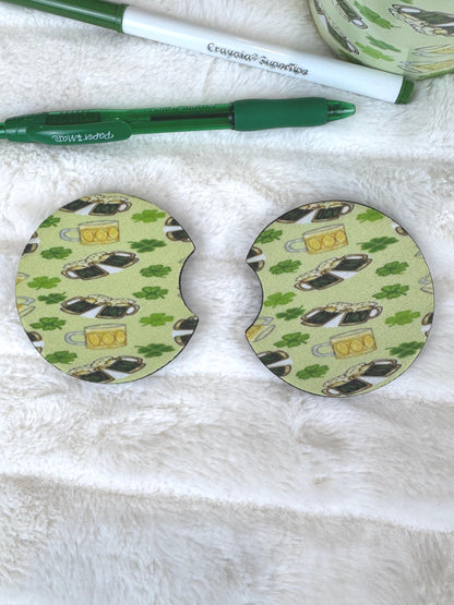 Two circular coasters with a St. Patrick's Day theme, featuring a green and beige pattern of shamrocks, leprechauns, and beer mugs, displayed on a white faux fur surface next to a green pen.