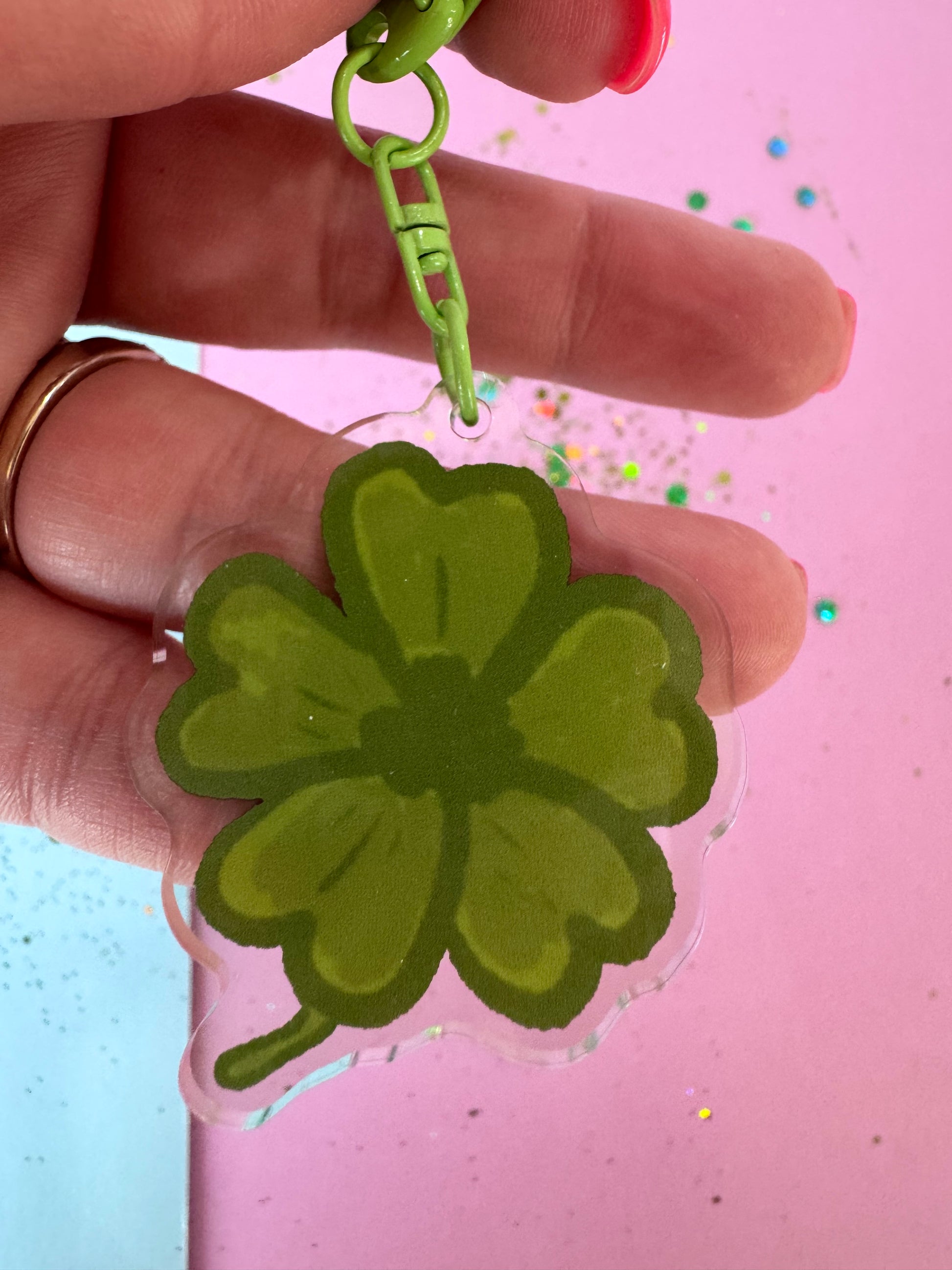 Green four-leaf clover keychain held by a hand against a pink background