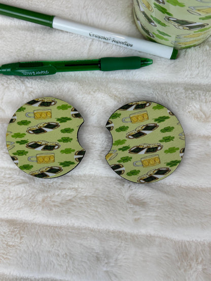 Two round coasters with a St. Patrick's Day coffee cup and clover pattern, displayed on a white faux fur surface next to a green pen and a matching patterned mug.